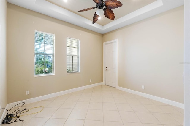 empty room with light tile patterned floors, a tray ceiling, and ceiling fan