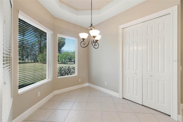 unfurnished dining area featuring light tile patterned floors, a notable chandelier, and a raised ceiling