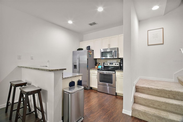 kitchen with a breakfast bar, light stone counters, appliances with stainless steel finishes, kitchen peninsula, and white cabinets