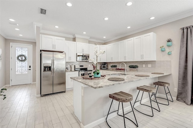 kitchen featuring a kitchen bar, sink, appliances with stainless steel finishes, kitchen peninsula, and white cabinets