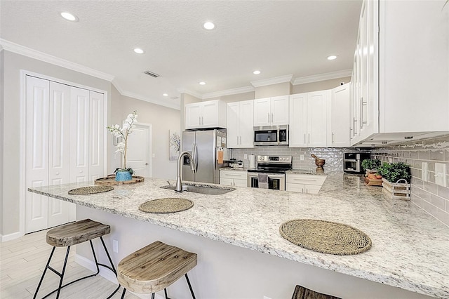 kitchen featuring white cabinets, a kitchen breakfast bar, kitchen peninsula, stainless steel appliances, and light stone countertops