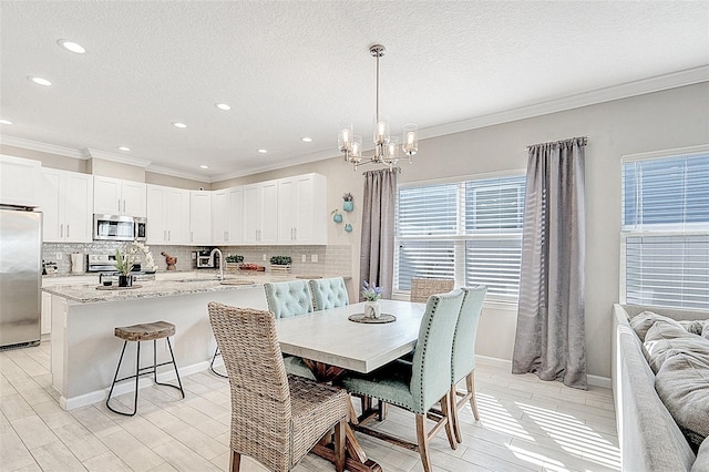 dining area featuring an inviting chandelier, ornamental molding, sink, and a textured ceiling