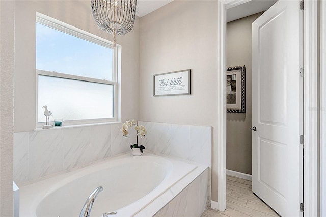 bathroom featuring tiled bath and a notable chandelier