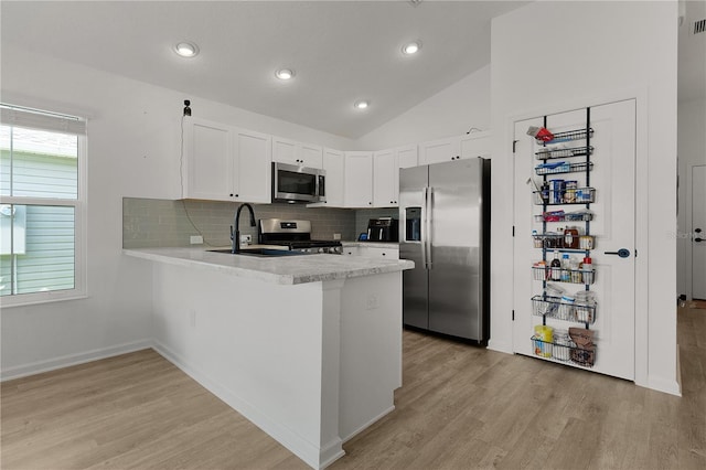 kitchen featuring appliances with stainless steel finishes, white cabinets, lofted ceiling, light hardwood / wood-style floors, and sink