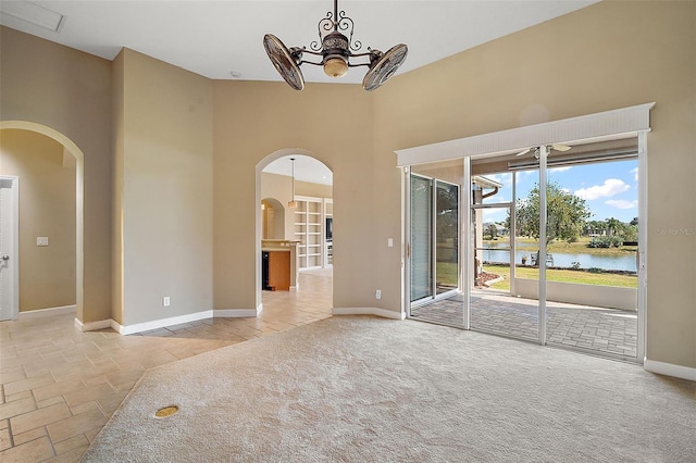 carpeted spare room with an inviting chandelier, a high ceiling, and a water view