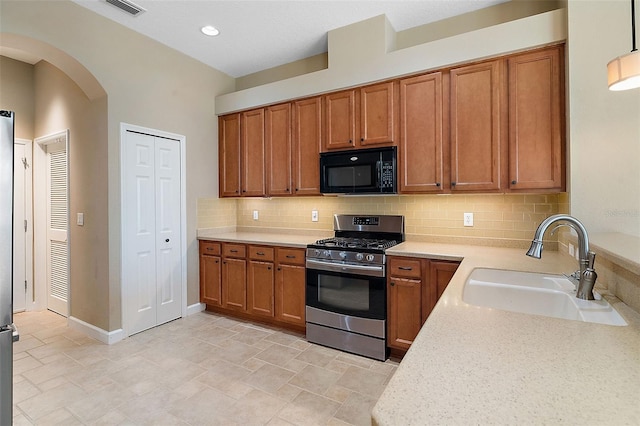 kitchen with sink, decorative backsplash, stainless steel gas range oven, and light stone countertops