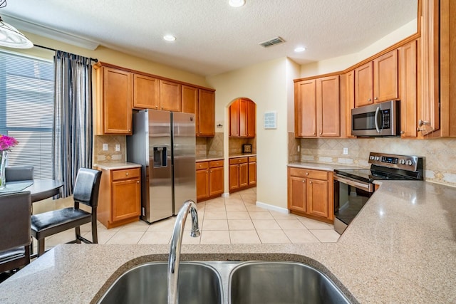 kitchen with light tile patterned flooring, sink, light stone counters, tasteful backsplash, and appliances with stainless steel finishes