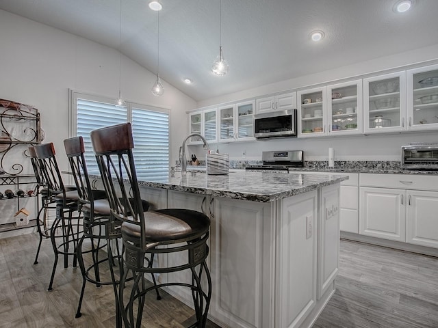 kitchen with pendant lighting, stone countertops, white cabinetry, stainless steel appliances, and a center island with sink