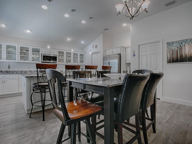 dining room with a notable chandelier, light hardwood / wood-style flooring, and vaulted ceiling