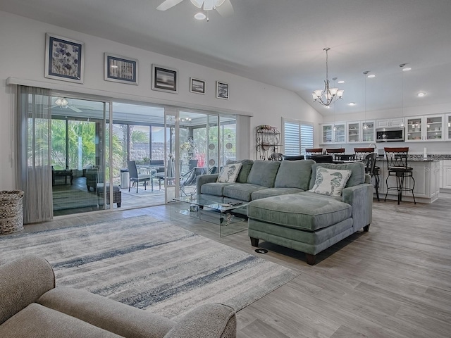 living room featuring ceiling fan with notable chandelier, vaulted ceiling, and light wood-type flooring