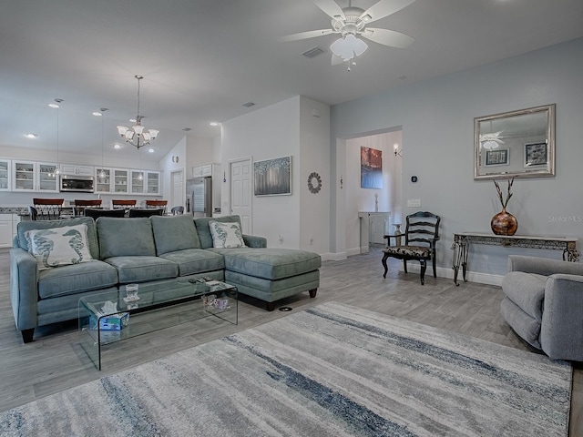 living room featuring vaulted ceiling, ceiling fan with notable chandelier, and light wood-type flooring