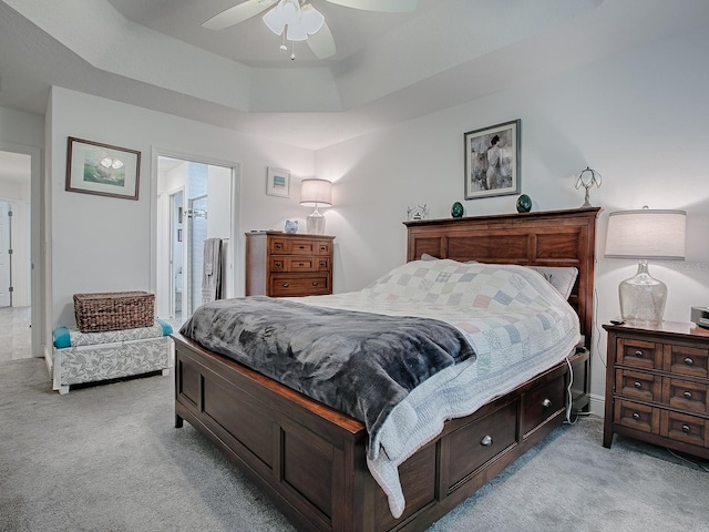 bedroom with connected bathroom, light colored carpet, ceiling fan, and a tray ceiling