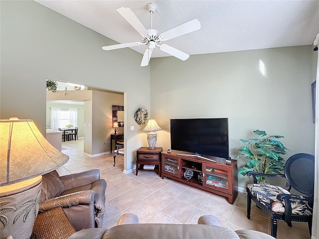 tiled living room featuring ceiling fan, high vaulted ceiling, and a textured ceiling