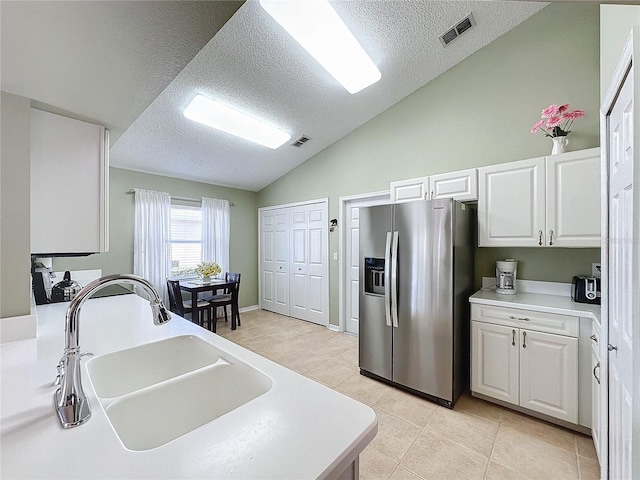 kitchen with sink, white cabinetry, vaulted ceiling, light tile patterned floors, and stainless steel fridge