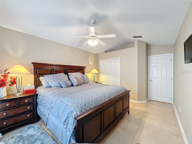 bedroom with lofted ceiling, a textured ceiling, light tile patterned floors, a closet, and ceiling fan