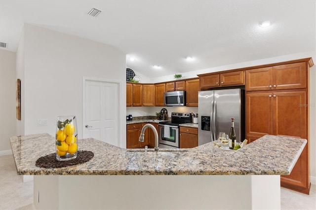 kitchen featuring sink, light stone counters, vaulted ceiling, appliances with stainless steel finishes, and an island with sink