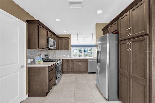 kitchen with light tile patterned floors, decorative backsplash, dark brown cabinets, and stainless steel appliances