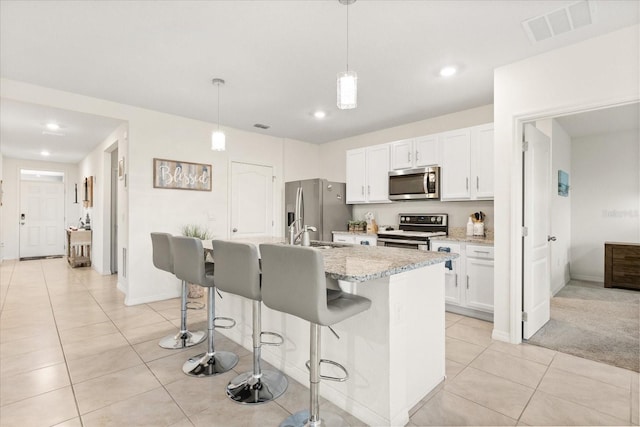 kitchen with white cabinetry, appliances with stainless steel finishes, decorative light fixtures, and a center island with sink