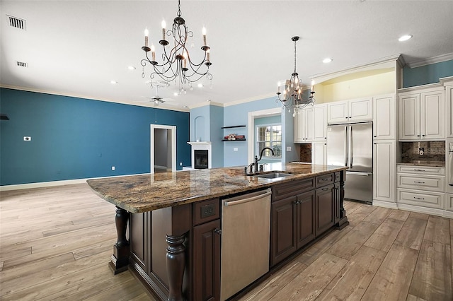 kitchen with visible vents, an island with sink, ornamental molding, stainless steel appliances, and a sink