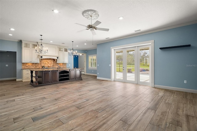 kitchen with baseboards, ornamental molding, open floor plan, light wood-type flooring, and backsplash