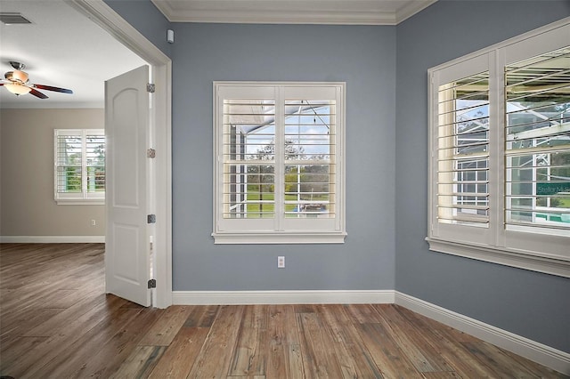 spare room featuring baseboards, visible vents, a ceiling fan, wood finished floors, and crown molding