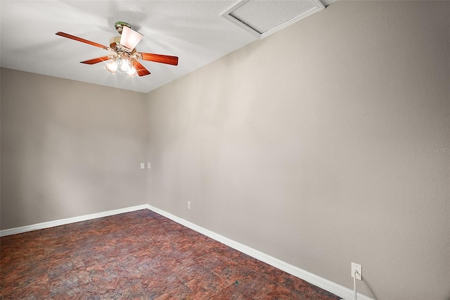 spare room featuring stone finish floor, attic access, baseboards, and a ceiling fan