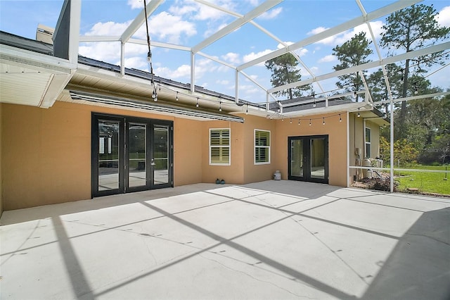 rear view of house with glass enclosure, french doors, a patio area, and stucco siding