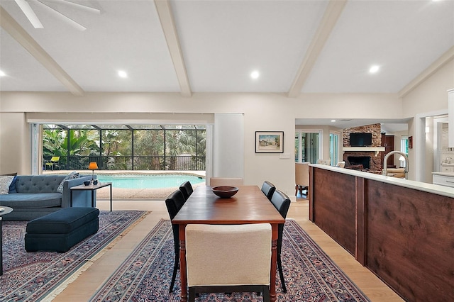 dining area featuring beam ceiling, sink, a stone fireplace, and light hardwood / wood-style flooring