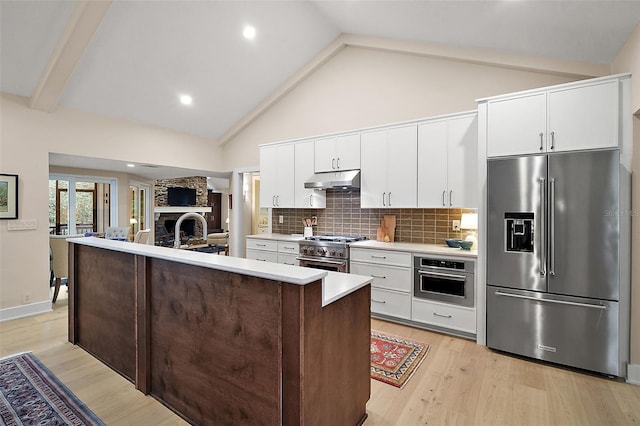 kitchen with an island with sink, a stone fireplace, premium appliances, and light hardwood / wood-style floors