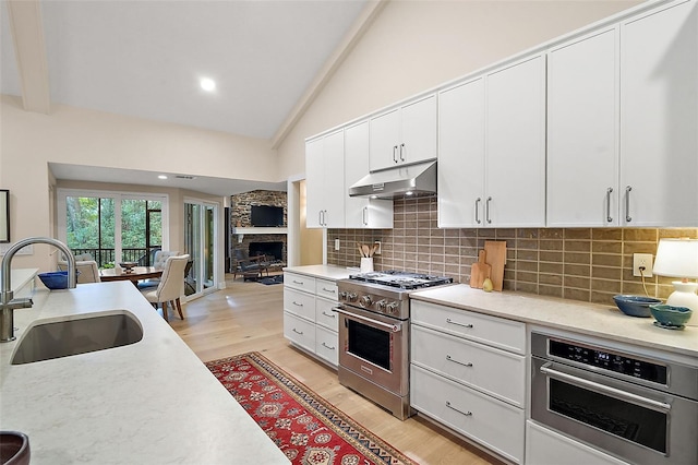 kitchen with appliances with stainless steel finishes, beamed ceiling, white cabinetry, sink, and light hardwood / wood-style floors