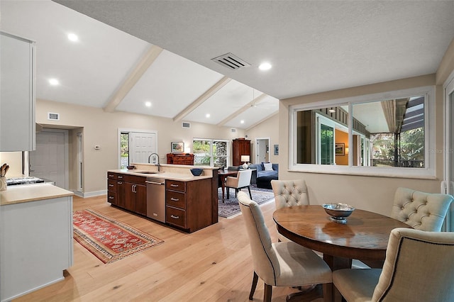 dining room featuring lofted ceiling with beams, sink, and light hardwood / wood-style flooring