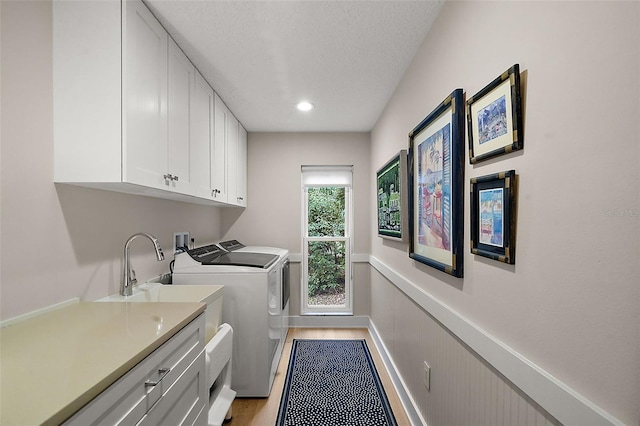 clothes washing area with sink, light wood-type flooring, cabinets, washing machine and dryer, and a textured ceiling