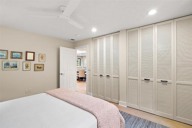 bedroom featuring multiple closets, ceiling fan, a textured ceiling, and light hardwood / wood-style flooring