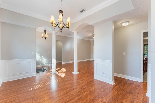 empty room featuring crown molding, hardwood / wood-style flooring, ceiling fan with notable chandelier, and ornate columns