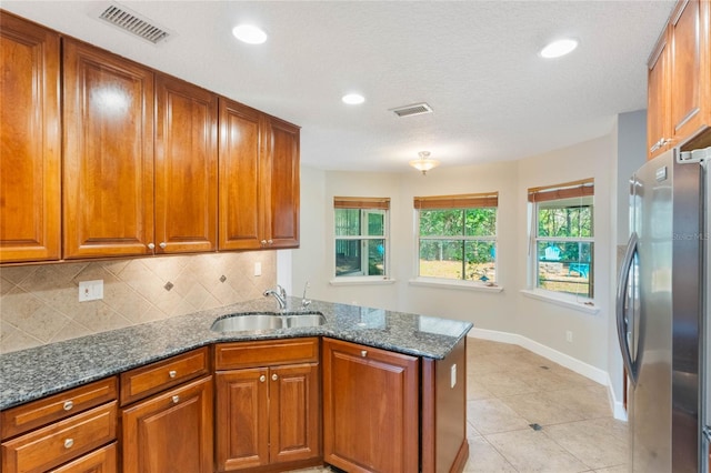 kitchen with sink, stainless steel fridge, backsplash, kitchen peninsula, and dark stone counters