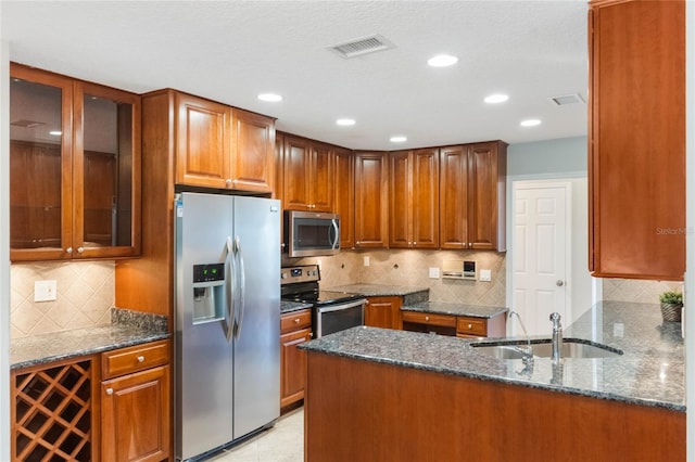 kitchen with dark stone countertops, sink, stainless steel appliances, and kitchen peninsula