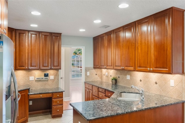 kitchen with sink, light tile patterned floors, dark stone countertops, stainless steel refrigerator with ice dispenser, and kitchen peninsula