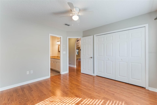 unfurnished bedroom featuring ensuite bath, a textured ceiling, light hardwood / wood-style flooring, a closet, and ceiling fan