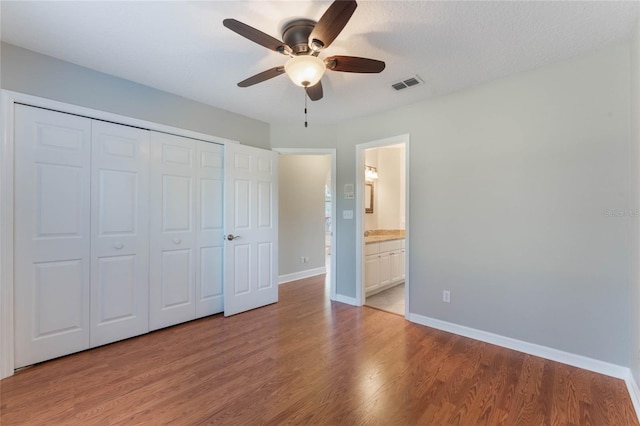 unfurnished bedroom featuring connected bathroom, a textured ceiling, light wood-type flooring, a closet, and ceiling fan