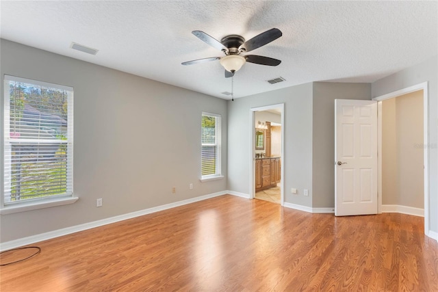 unfurnished bedroom featuring ceiling fan, ensuite bath, a textured ceiling, and light wood-type flooring