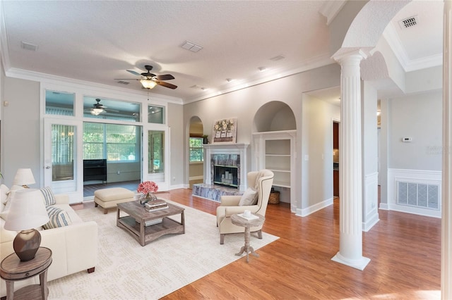 living room with ornate columns, a fireplace, crown molding, a textured ceiling, and light wood-type flooring