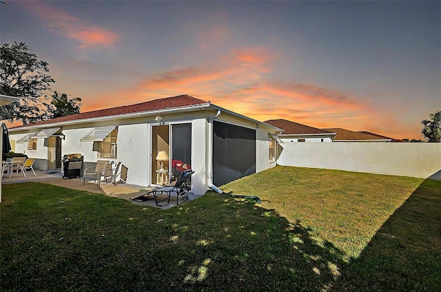 back house at dusk with a patio and a lawn