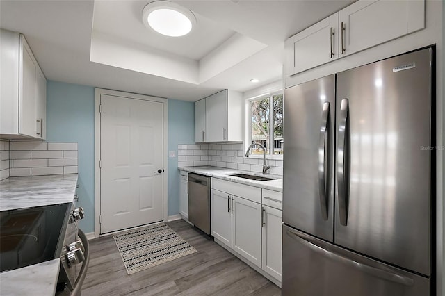 kitchen with appliances with stainless steel finishes, a raised ceiling, sink, and white cabinets