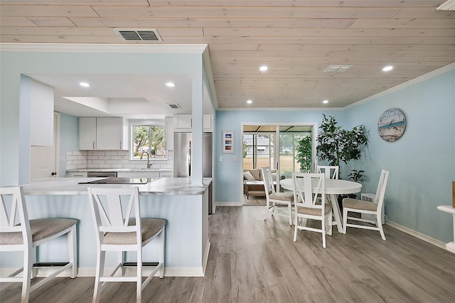 kitchen featuring crown molding, stainless steel refrigerator, white cabinetry, decorative backsplash, and kitchen peninsula