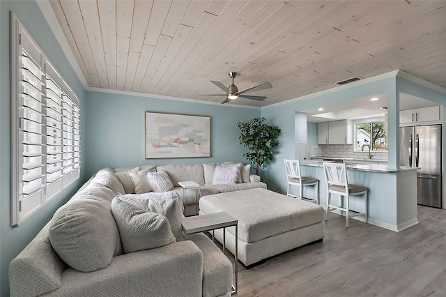 living room with sink, crown molding, wooden ceiling, and light wood-type flooring