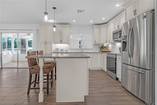 kitchen with white cabinetry, light stone counters, a center island, appliances with stainless steel finishes, and pendant lighting