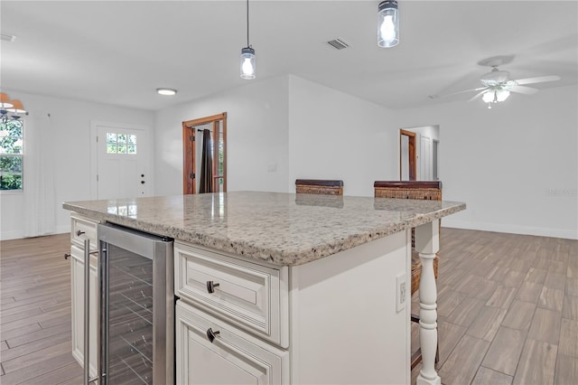 kitchen with wine cooler, light stone counters, hanging light fixtures, light hardwood / wood-style flooring, and a kitchen island