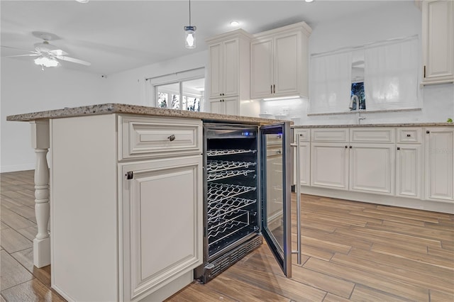 kitchen featuring light hardwood / wood-style flooring, white cabinetry, light stone counters, decorative light fixtures, and beverage cooler