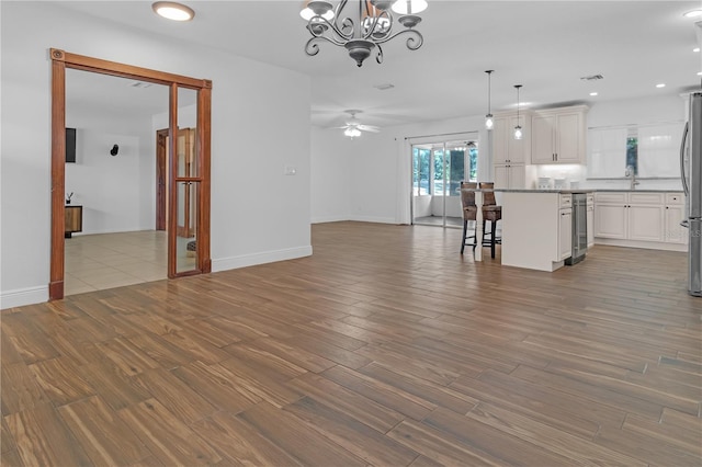 unfurnished living room featuring wine cooler, sink, hardwood / wood-style flooring, and ceiling fan with notable chandelier