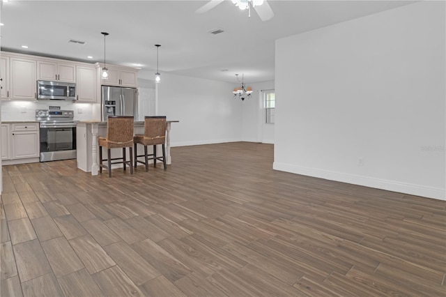 kitchen featuring a breakfast bar area, appliances with stainless steel finishes, white cabinetry, a kitchen island, and decorative light fixtures